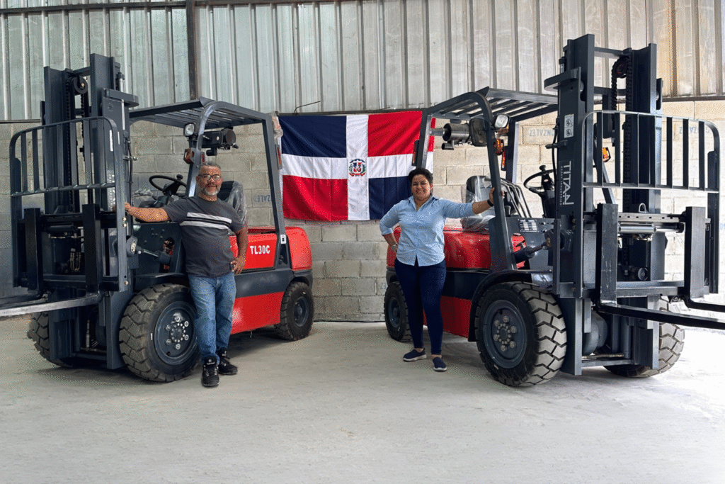 Dos personas posando junto a montacargas en almacén con bandera dominicana al fondo